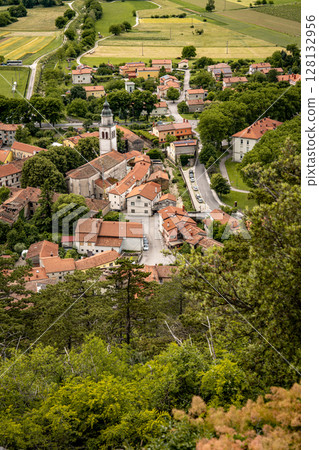 Picturesque View Of Vipava From Castle Ruins: Red-Tiled Rooftops And Church Tower Nestled In Green Valley With Blooming Flowers In Foreground And Rolling Fields In Background, Slovenia 128132956