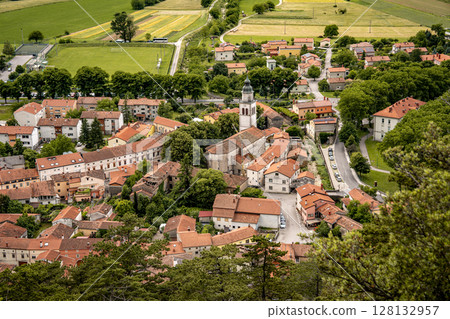 Picturesque View Of Vipava From Castle Ruins: Red-Tiled Rooftops And Church Tower Nestled In Green Valley With Blooming Flowers In Foreground And Rolling Fields In Background, Slovenia 128132957