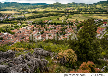 Picturesque View Of Vipava From Castle Ruins: Red-Tiled Rooftops And Church Tower Nestled In Green Valley With Blooming Flowers In Foreground And Rolling Fields In Background, Slovenia 128132962