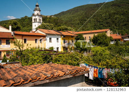 Charming Townscape Of Vipava With Castle View: Colorful Historic Houses And Church Tower Nestled Below Forested Hills With Distant Castle Ruins Under A Clear Blue Sky In Western Slovenia 128132963
