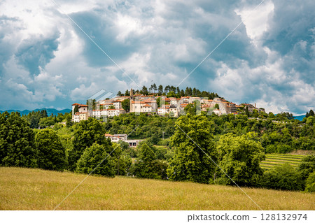 Scenic Hilltop Town Of Stanjel In Slovenia: Traditional Stone Houses And Historic Church Tower Rising Above Lush Greenery Under A Dramatic Cloudy Sky In The Karst Region Scenic Hilltop Town Of Stanjel In Slovenia: Traditional Stone Houses And Historic Church Tower Rising Above Lush Greenery Under A Dramatic Cloudy Sky In The Karst Region 128132974