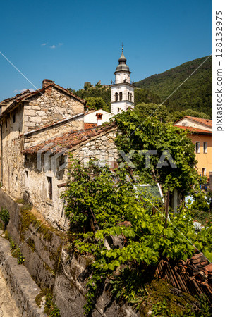 Charming Townscape Of Vipava With Castle View: Colorful Historic Houses And Church Tower Nestled Below Forested Hills With Distant Castle Ruins Under A Clear Blue Sky In Western Slovenia 128132975