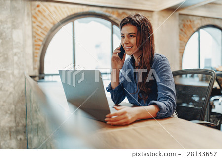 A Professional Woman Actively Engaged in Her Work Remotely with a Laptop and Phone Nearby A Professional Woman Actively Engaged in Her Work Remotely with a Laptop and Phone Nearby 128133657