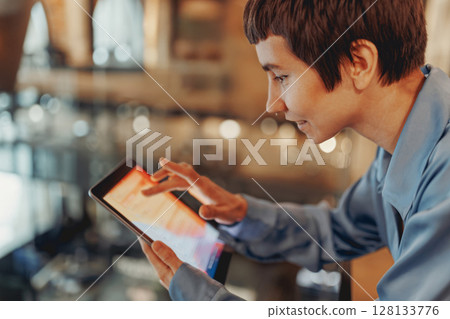 Young Professional Engaged with Tablet in Modern Caf Setting Young Professional Engaged with Tablet in Modern Caf Setting 128133776