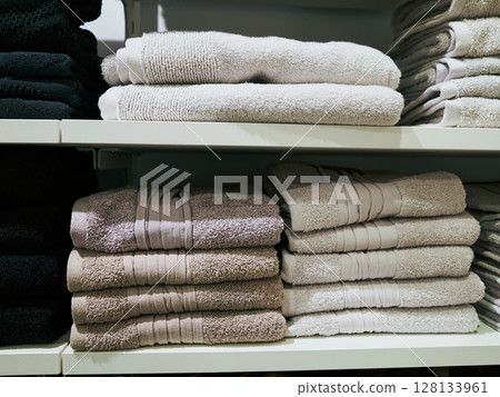 White and tan stack of towels sits on a shelf next to a black stack 128133961