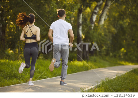Sport workout and outdoor run of active couple, two people jogging in summer park in morning Sport workout and outdoor run of active couple, two people jogging in summer park in morning 128134539