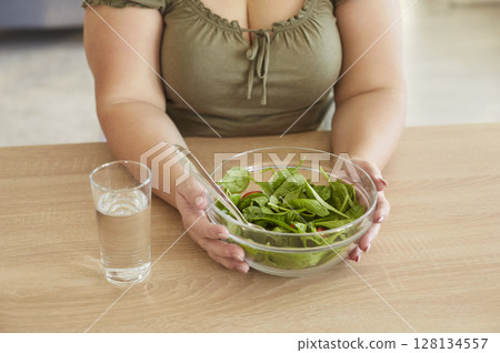 Healthy slimming vegetarian diet, salad in bowl, water glass, woman eating green vegetables 128134557