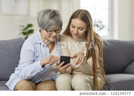 Mother And Adult Daughter Enjoying Online Leisure On Phone At Home Mother And Adult Daughter Enjoying Online Leisure On Phone At Home 128134577