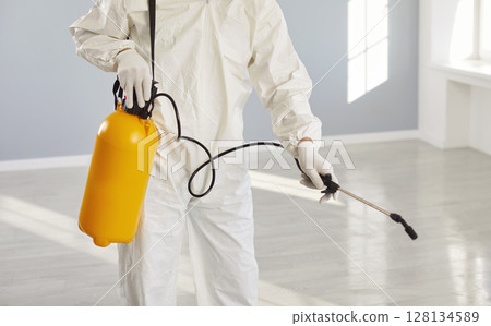 Exterminator service man, worker wearing protective white coverall holding pump sprayer  128134589
