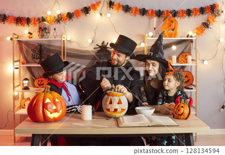 Happy family curving pumpkin for Halloween, wearing festive costumes preparing for holiday 128134594