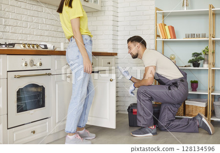 Professional man plumber fixing problems with sink, clogged drain, woman client standing near 128134596