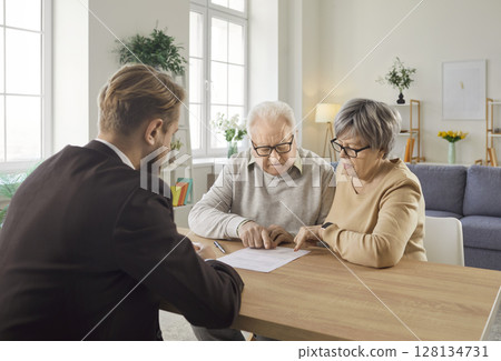 Senior couple sitting at table and studying terms of health insurance contract with financial agent. Senior couple sitting at table and studying terms of health insurance contract with financial agent. 128134731