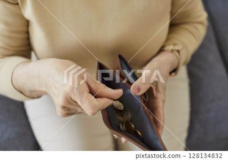 Senior elderly woman putting coins into open wallet sitting on sofa in living room at home Senior elderly woman putting coins into open wallet sitting on sofa in living room at home 128134832