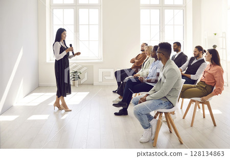 Female speaker holding a microphone and giving a lecture for young diverse people 128134863
