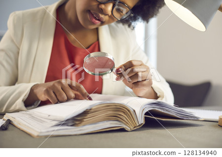 Young african american Bbusiness woman reading looking through magnifying glass 128134940