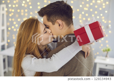 Side view of a beautiful young woman kissing her husband on the cheek in gratitude for a gift. Side view of a beautiful young woman kissing her husband on the cheek in gratitude for a gift. 128134943