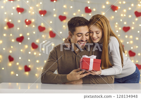 Loving young woman giving present to her boyfriend on Saint Valentine's Day or anniversary 128134948