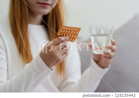 Young Woman Holding Birth Control Pills and a Glass of Water, Concept of Contraception and Family Planning Young Woman Holding Birth Control Pills and a Glass of Water, Concept of Contraception and Family Planning 128135442