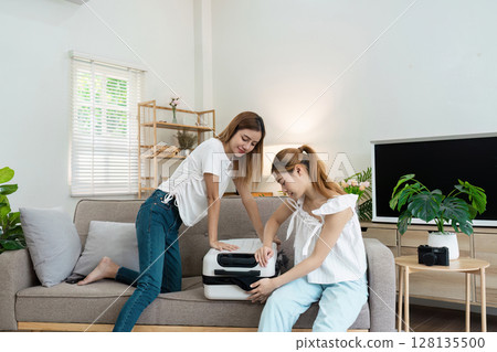 Two Young Women Packing Suitcase for Travel Adventure in Cozy Living Room 128135500