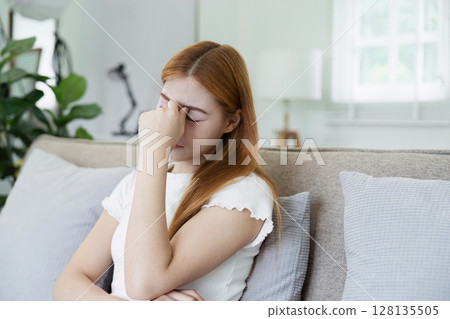 Young Woman Suffering from Headache Sitting on Couch at Home, Stress and Pain Concept 128135505