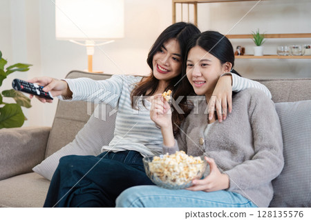 Happy LGBT Couple Relaxing at Home, Watching TV and Enjoying Popcorn Together in a Cozy Living Room Setting, Embracing Love and Togetherness, Celebrating Modern Lifestyle and Inclusivity Happy LGBT Couple Relaxing at Home, Watching TV and Enjoying Popcorn Together in a Cozy Living Room Setting, Embracing Love and Togetherness, Celebrating Modern Lifestyle and Inclusivity 128135576