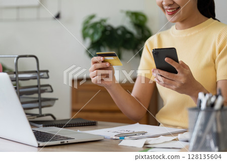 Woman Shopping Online with Credit Card and Mobile at Home Office Desk, Smiling and Enjoying Convenient Digital Payment, Modern Technology for Secure Online Transactions Woman Shopping Online with Credit Card and Mobile at Home Office Desk, Smiling and Enjoying Convenient Digital Payment, Modern Technology for Secure Online Transactions 128135604