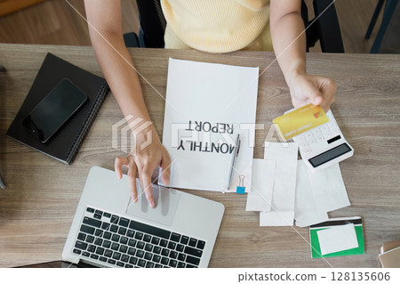 Woman Using Credit Card for Online Payment with Laptop and Monthly Report on Desk - Financial Management and E-commerce Concept 128135606