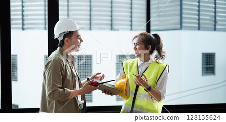 Professional Engineers Collaborating on Construction Project in Modern Office Setting with Safety Gear and Blueprints Professional Engineers Collaborating on Construction Project in Modern Office Setting with Safety Gear and Blueprints 128135624