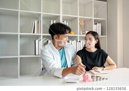 Young Couple Discussing Savings and Bills at Home with Piggy Bank and Coins on Table, Financial Planning, Budgeting, and Money Management Concept 128135638