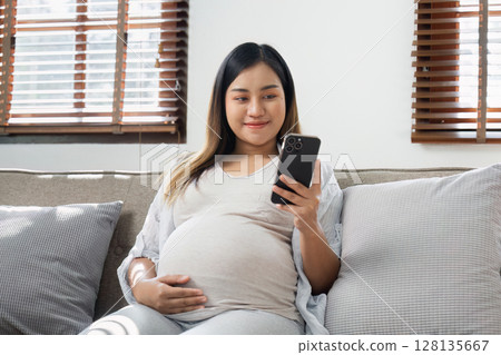 Pregnancy Enjoying Technology and comfortable at Home, Natural Light Through Window Blinds, Casual Maternity Lifestyle 128135667