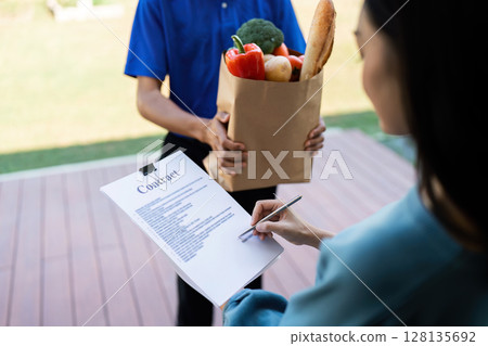 Home Delivery Service Customer Receiving Grocery Package and Signing for Delivery Confirmation 128135692