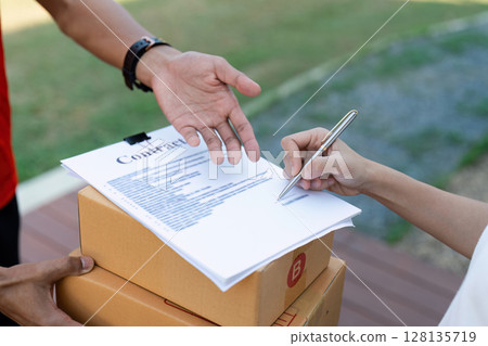 Close-Up of Delivery Service Transaction with Customer Signing for Package on Clipboard, Couriers Handing Over Parcels, Efficient and Reliable Shipping Concept, Outdoors 128135719