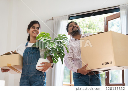 Indian Couple Moving into New Home, Carrying Boxes and Plant, Smiling and Excited, Bright and Modern Interior, Relocation and New Beginnings, Happy Homeowners, Diverse and Contemporary Lifestyle Indian Couple Moving into New Home, Carrying Boxes and Plant, Smiling and Excited, Bright and Modern Interior, Relocation and New Beginnings, Happy Homeowners, Diverse and Contemporary Lifestyle 128135832