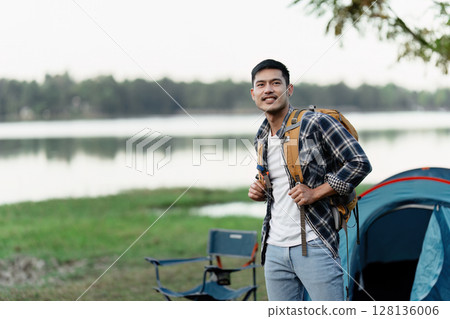 Young Adventurer Enjoying Travel Camping by the Lake with Backpack and Tent in Scenic Outdoors Setting Young Adventurer Enjoying Travel Camping by the Lake with Backpack and Tent in Scenic Outdoors Setting 128136006