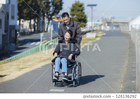 Husband assisting wife in wheelchair Husband assisting wife in wheelchair 128136292