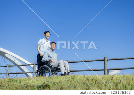 Senior male riding a wheelchair and a caregiver 128136362