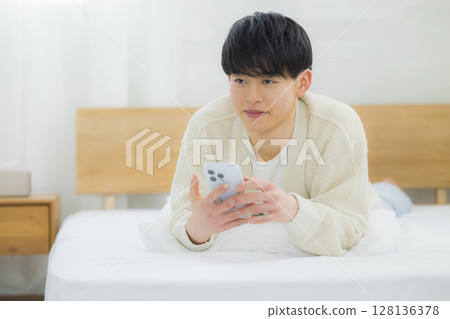 年輕人在床上使用智慧型手機 128136378