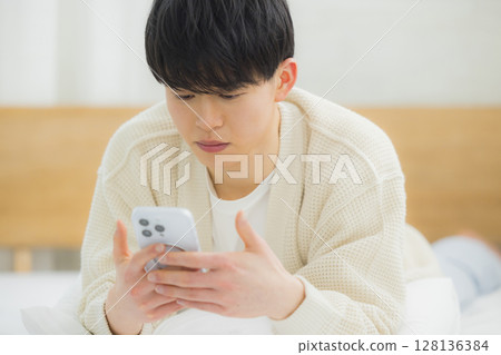 Young man using smartphone in bed Young man using smartphone in bed 128136384