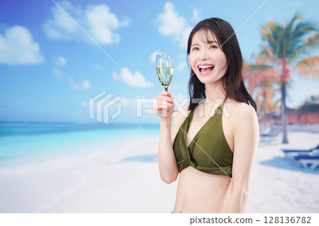 盛夏時節，身穿泳衣的年輕女子在沙灘上喝氣泡酒 128136782