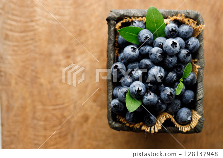 Ripe blueberries in wicker basket on wooden table. 128137948