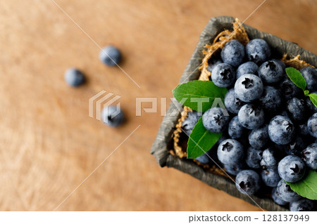 Ripe blueberries in wicker basket on wooden table. 128137949