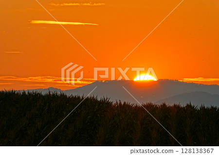 The sun slowly sinks behind the mountain and the crimson sky 128138367