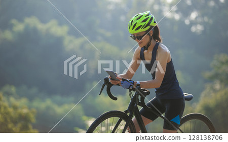 Woman cyclist using mobile phone in summer park Woman cyclist using mobile phone in summer park 128138706