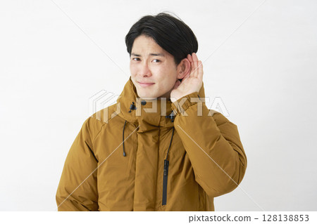 A man wearing a down jacket listening with his hand on his ear, white background 128138853