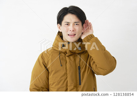 A man wearing a down jacket listening with his hand on his ear, white background 128138854