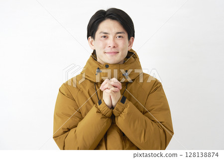 A man wearing a down jacket prays on a white background, looking at the camera A man wearing a down jacket prays on a white background, looking at the camera 128138874