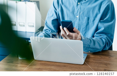 A man operating a smartphone and a computer 128140157