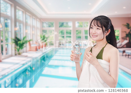 一名身穿泳衣的女子在泳池裡喝水降溫 128140368