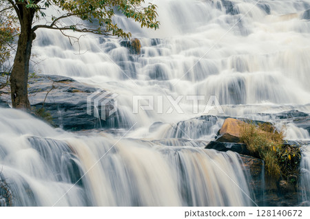 Beautiful waterfall with a lush green forest in the background. The water is flowing down the rocks and creating a beautiful scene. Sustainable waterfall in lush forest promoting water sustainability. 128140672