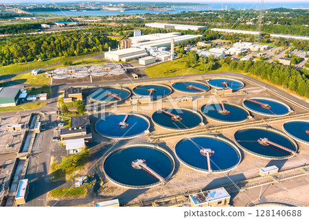 Aerial view of wastewater treatment plant with circular tanks, machinery, nearby greenery Aerial view of wastewater treatment plant with circular tanks, machinery, nearby greenery 128140688